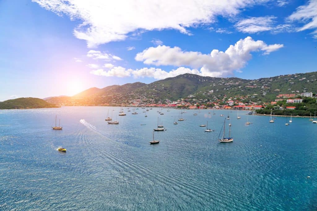 Scenic Caribbean harbor with sailboats and lush green hills at sunset.