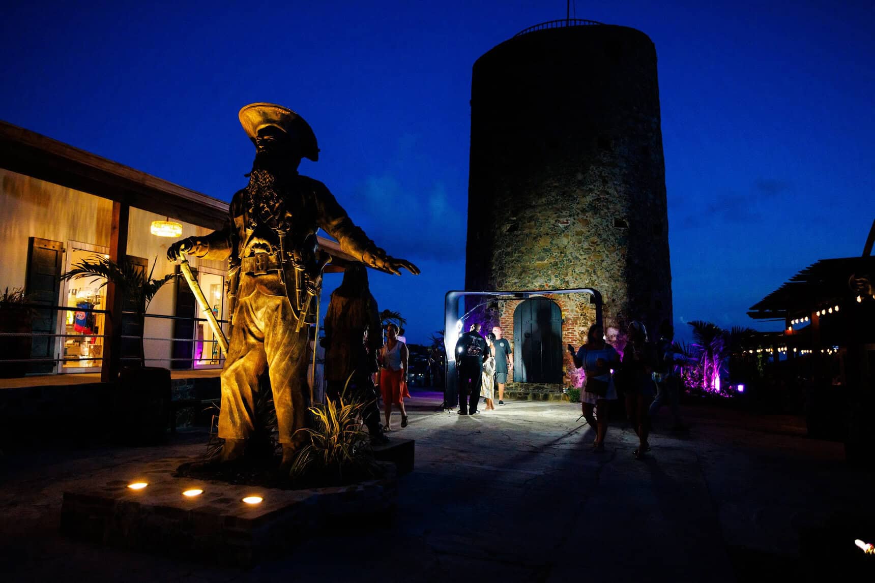 Illuminated pirate statue beside the historic Skytsborg stone tower at Blackbeard's Castle at blue hour